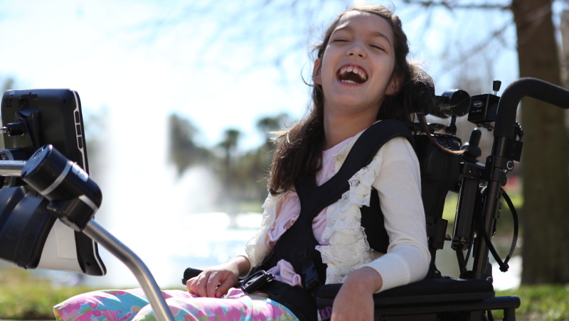 Image of Hannah, a client of Tobii ATI, in a wheelchair showing her communication device.